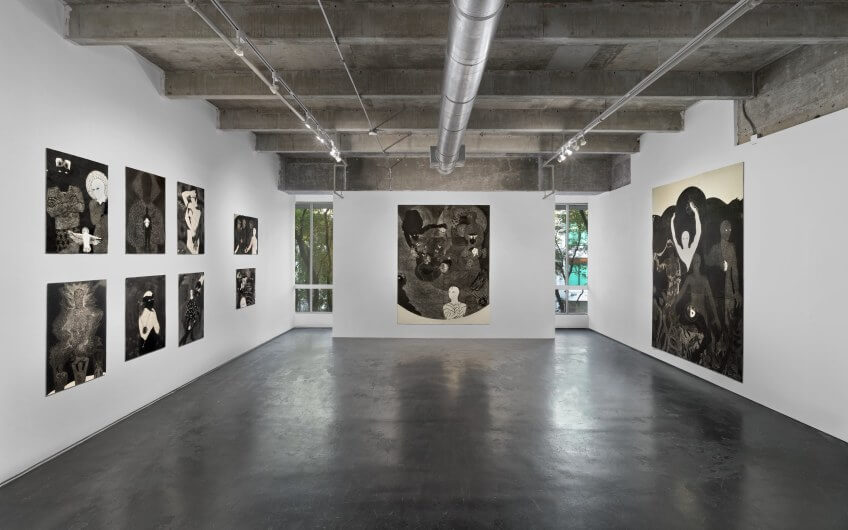 Black-and-white drawings and paintings with surreal themes in a minimalist gallery space during Miami Art Week.