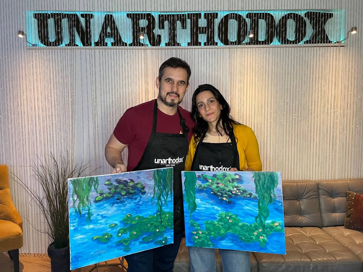 Couple holding their completed paintings at Unarthodox
